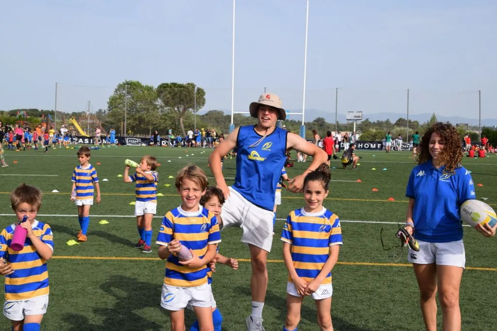 Niños y entrenadores participando en un festival de escuelas de rugby M12 en un campo al aire libre