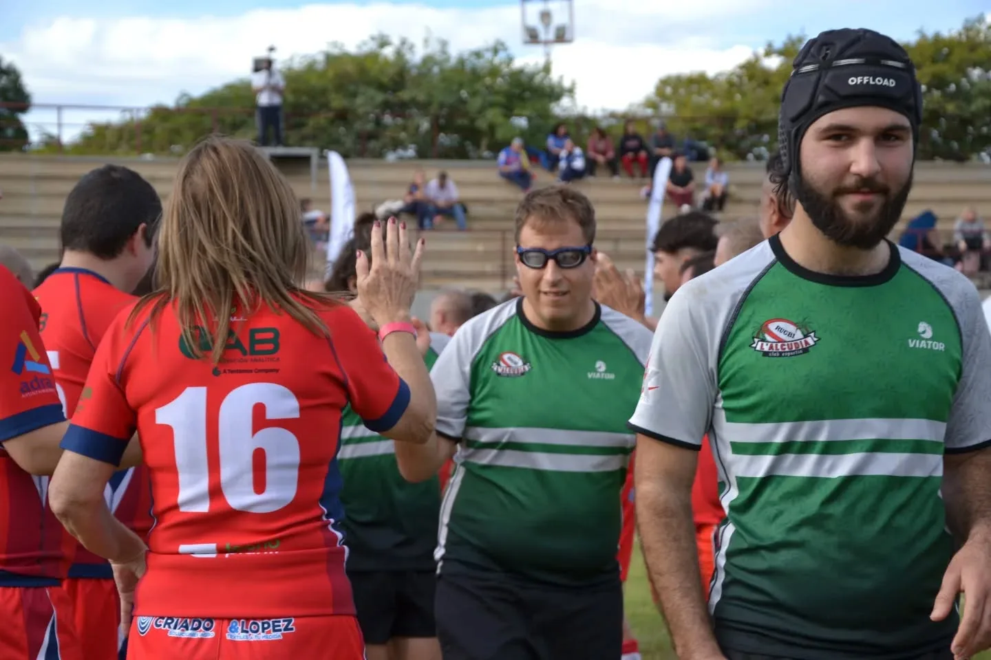 Jugadores de rugby inclusivo saludándose tras un partido durante un evento deportivo en un campo de rugby.